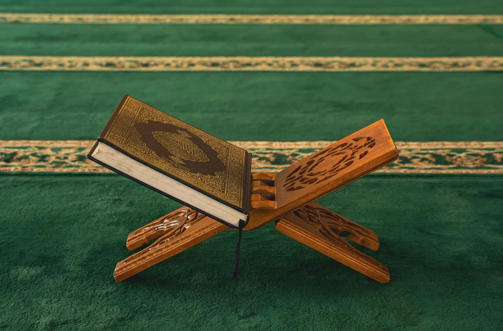 Quran resting on a wooden stand on a green prayer carpet