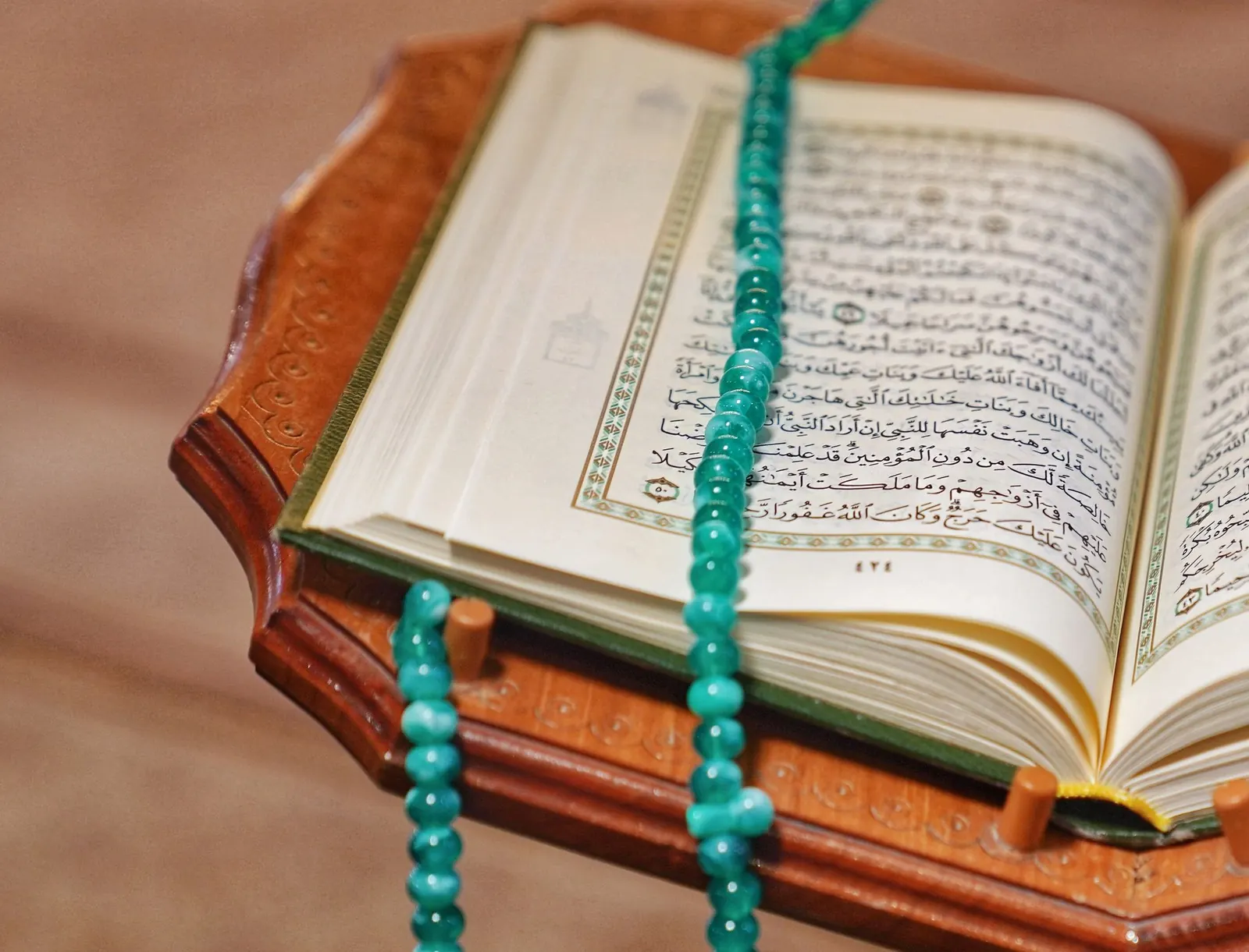 An open Quran with turquoise prayer beads resting on a wooden stand.