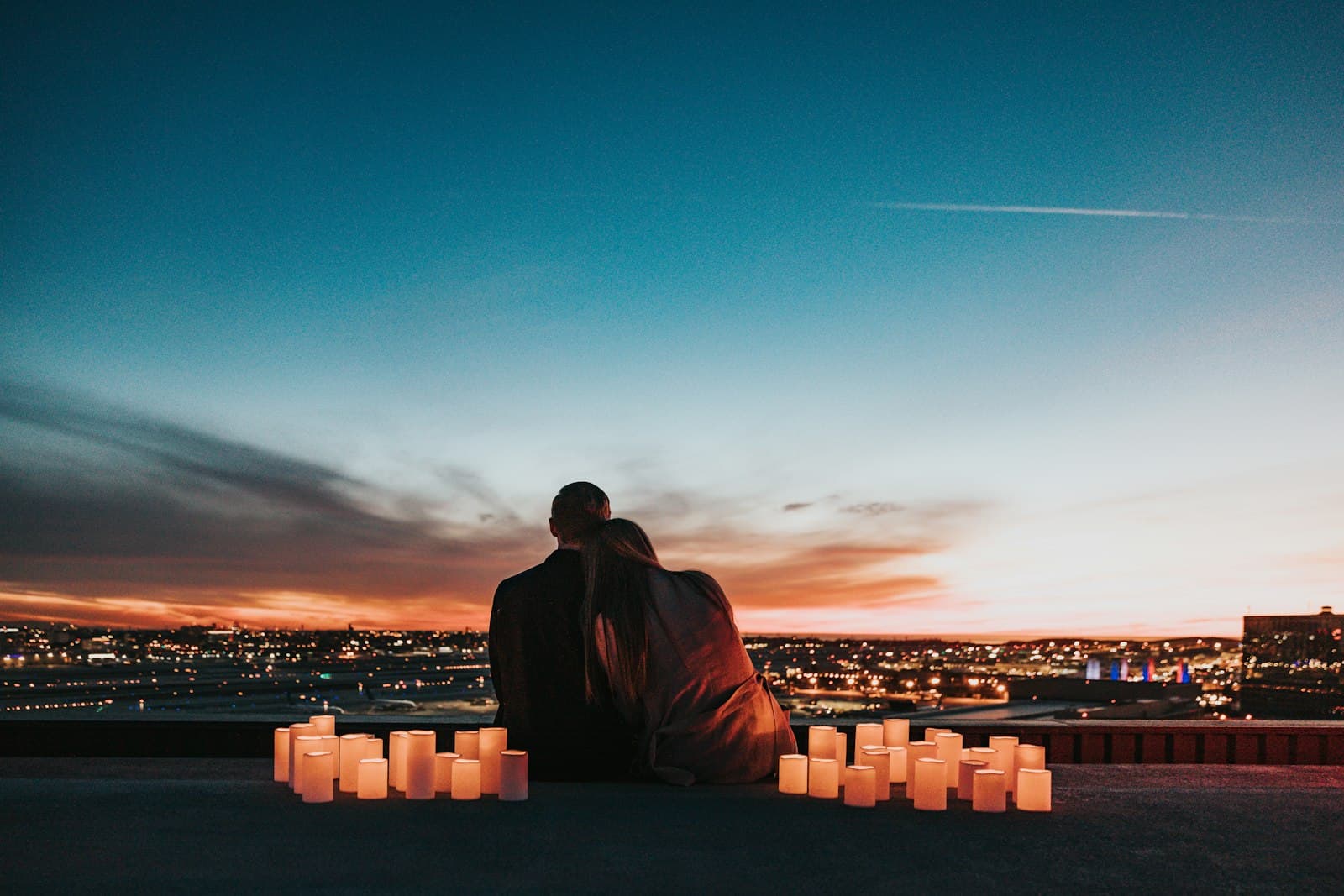 A couple sitting close together at sunset, with a city and candles in front of them