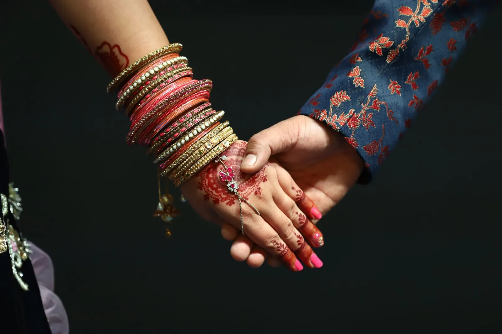 Close-up of two hands held together, decorated with henna designs and bracelets.