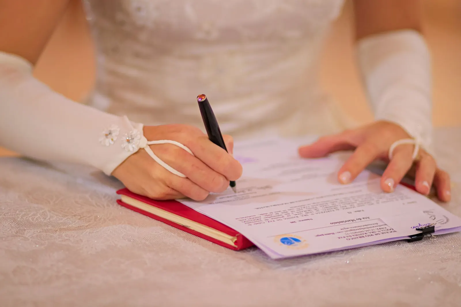 Close-up of a bride's hand signing a wedding certificate with a pen.