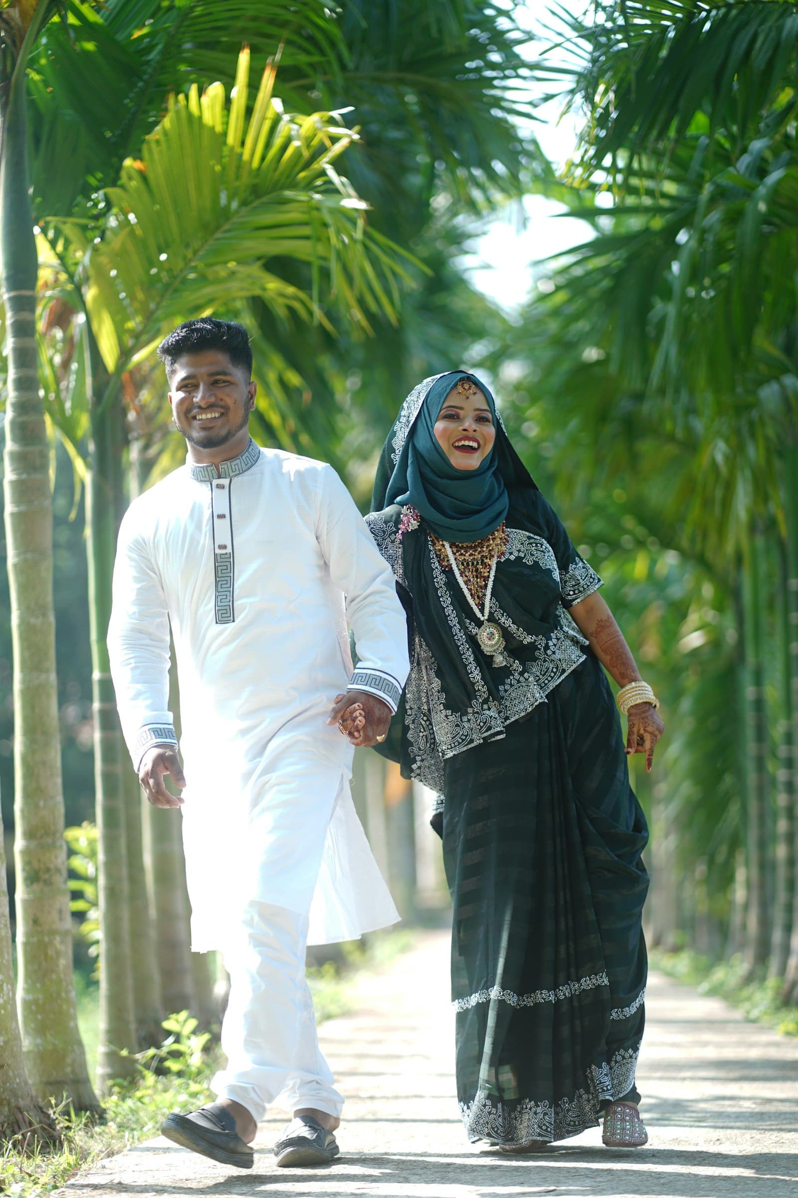 A smiling couple walking hand in hand, the groom in a white kurta
