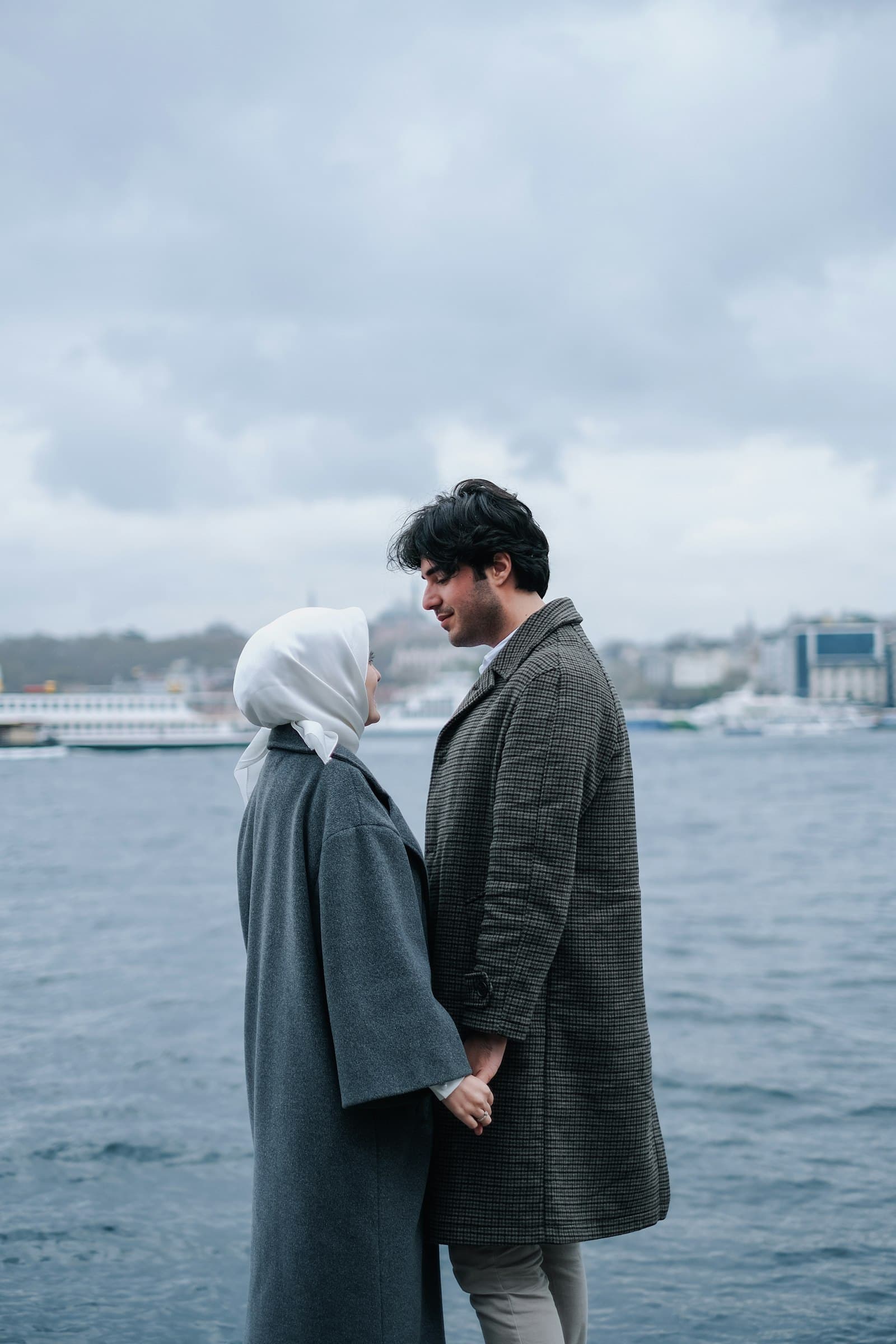 A couple standing by the water, the bride in a white headscarf