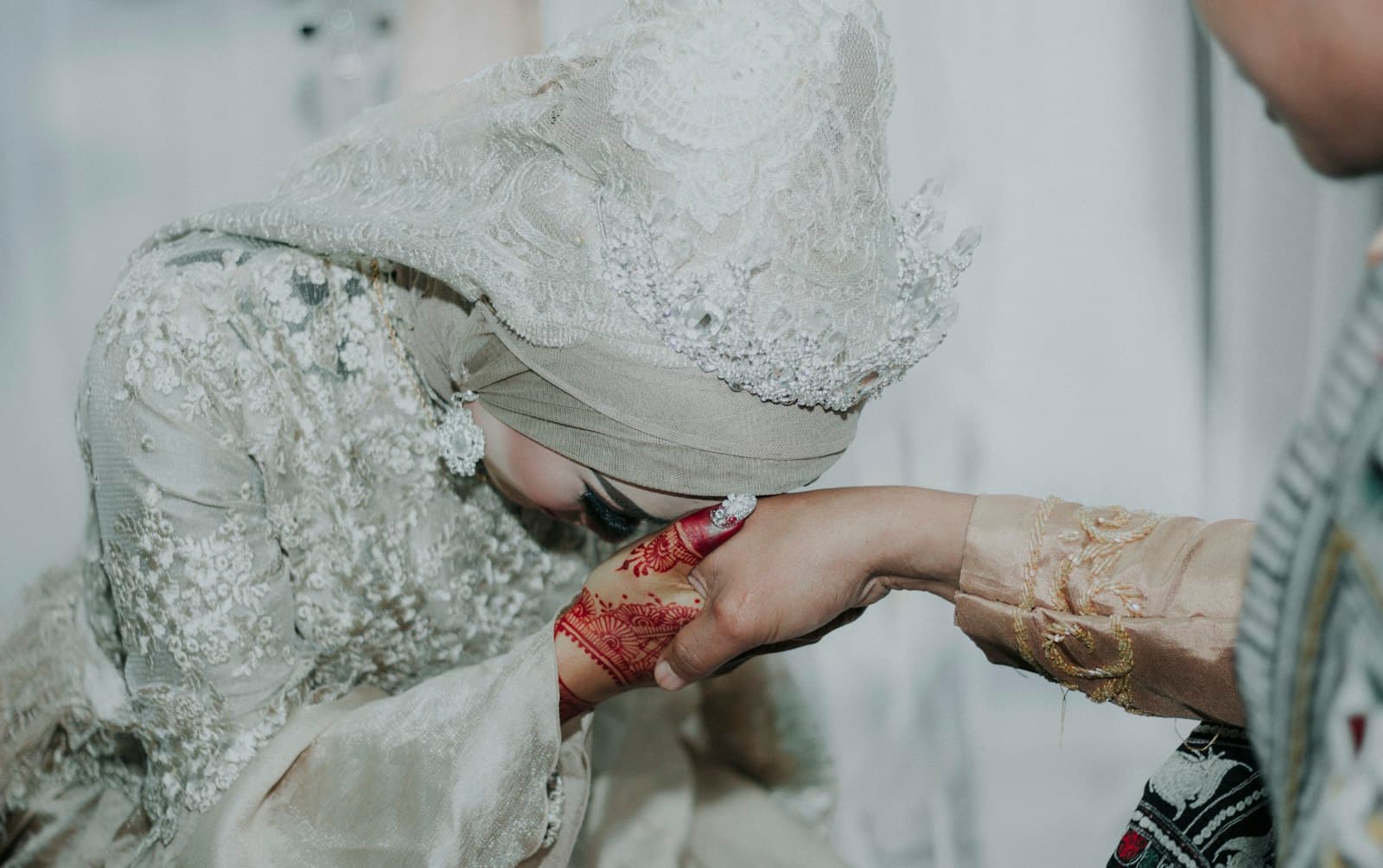 A bride in a lace veil kissing her groom's hand after the nikah