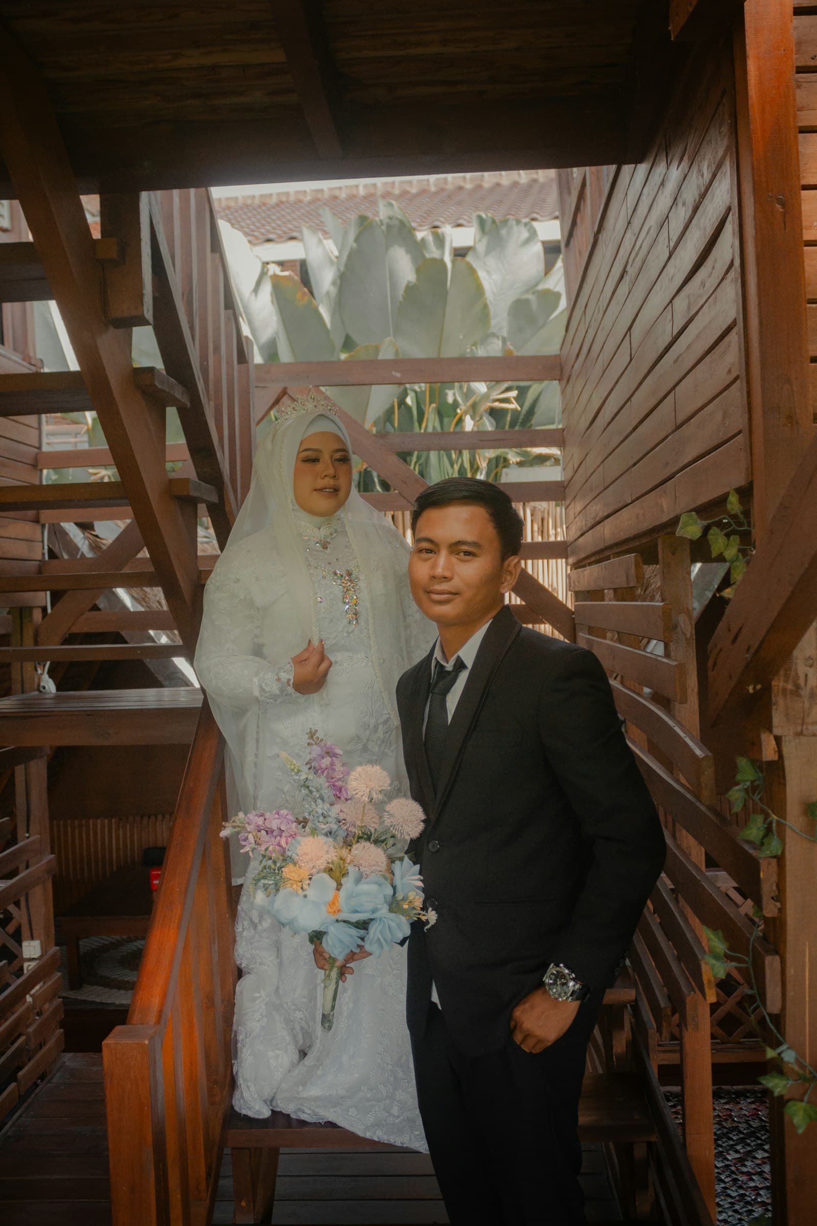 A bride in white and her groom posing together on a wooden staircase