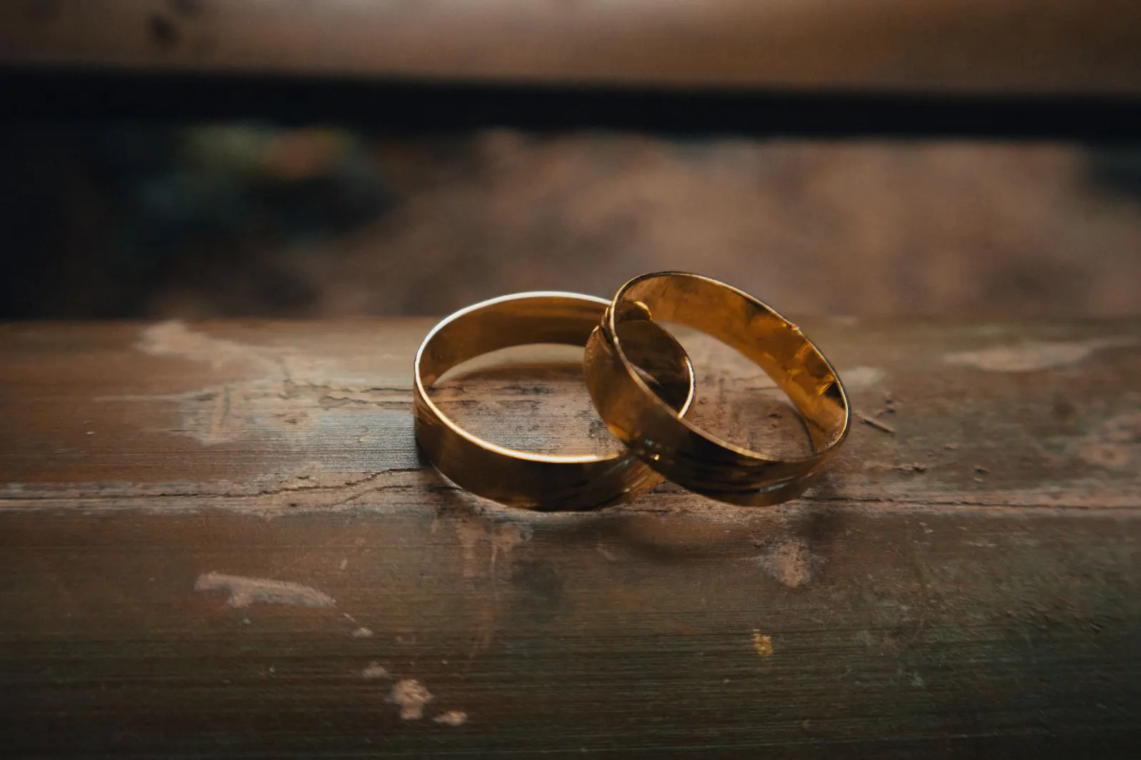 Two gold wedding rings resting on a rustic wooden table.