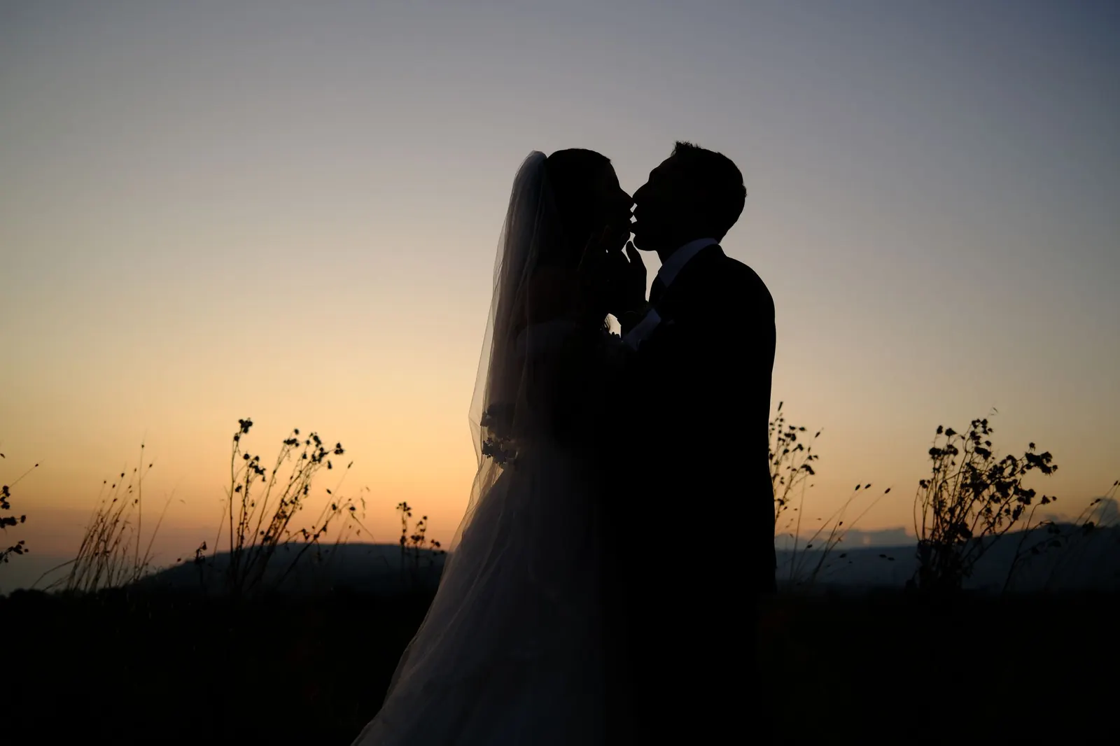 Silhouettes of a bride and groom against a sunset sky.