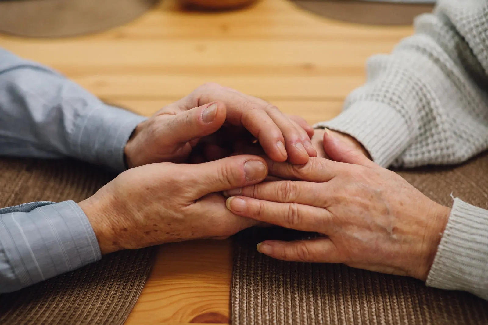 Elderly couple holding hands on a wooden table